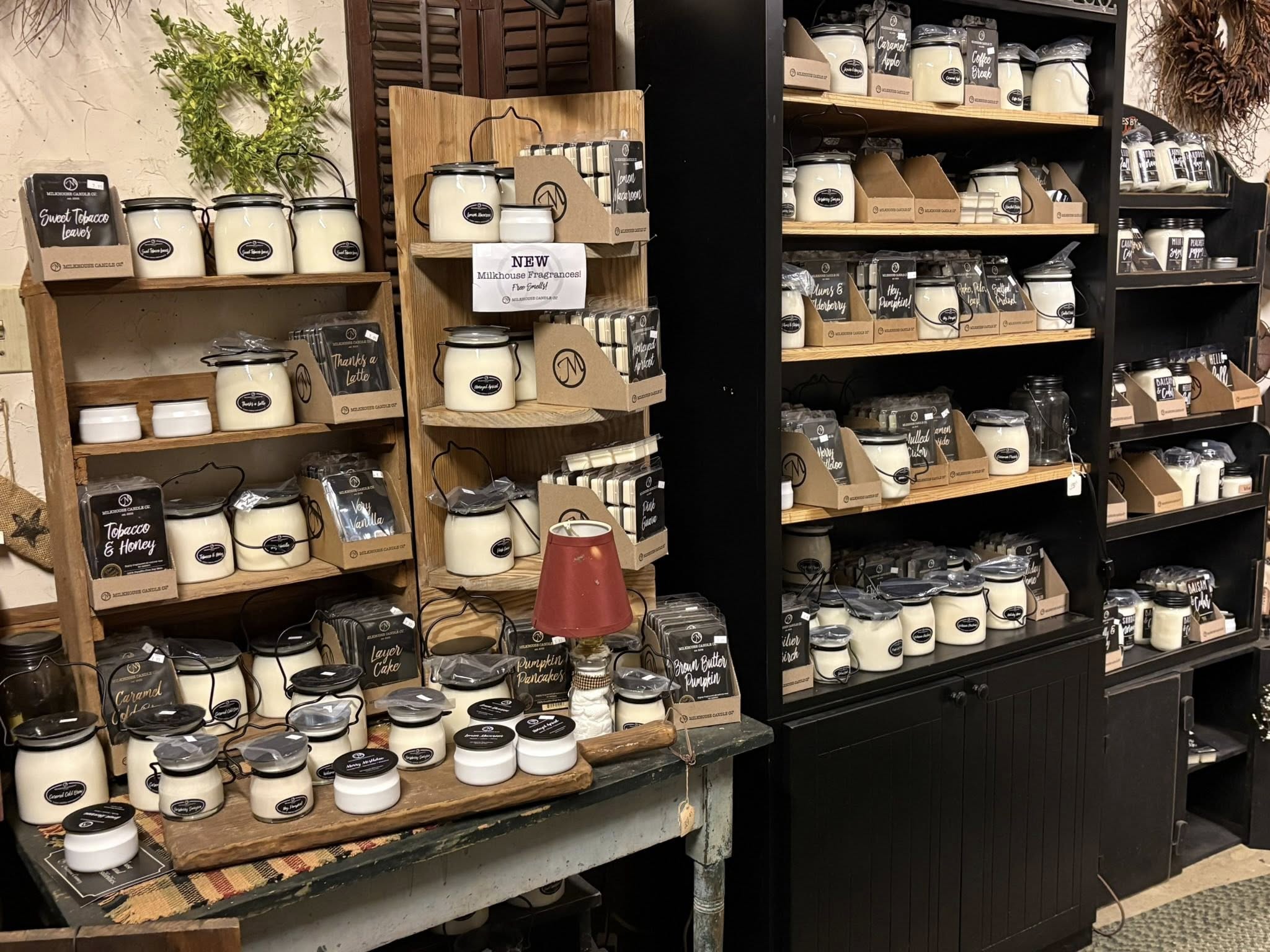 Full display of Milkhouse Candle Co. candles in various sizes and fragrances on rustic wooden shelving
