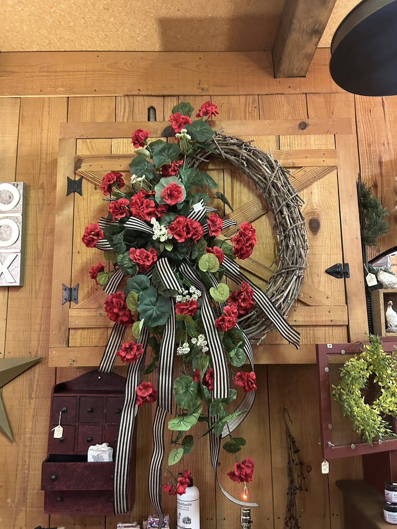Red geranium wreath on grapevine with striped ribbon