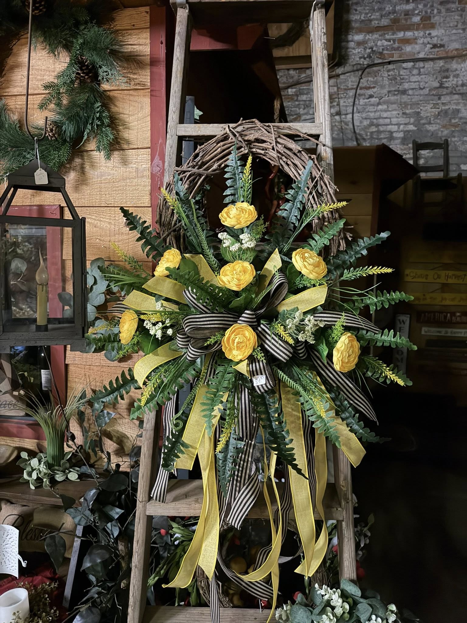Yellow ranunculus wreath with black and white striped ribbon on rustic ladder